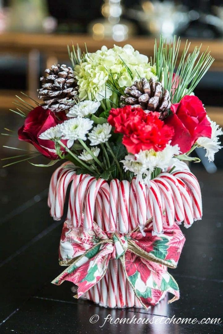 Close up of a small DIY red and white Christmas centerpiece made with candy canes, ribbon, flowers, pine needles and pine cones.