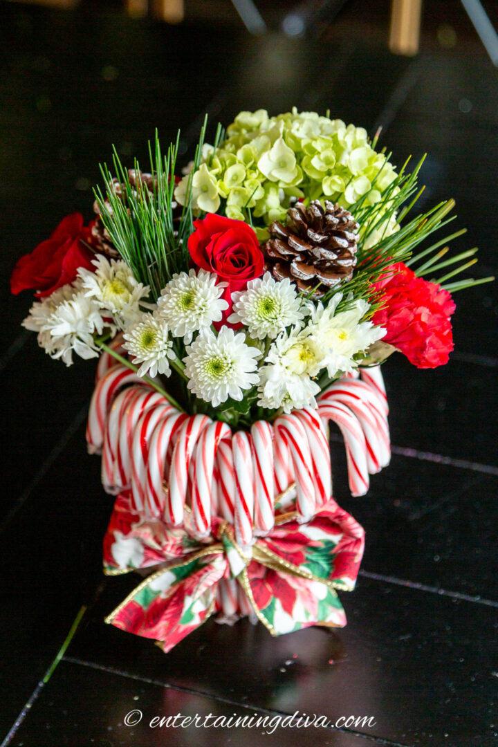 A candy cane Christmas centerpiece made with candy canes, red and white flowers, pine needles and pine cones