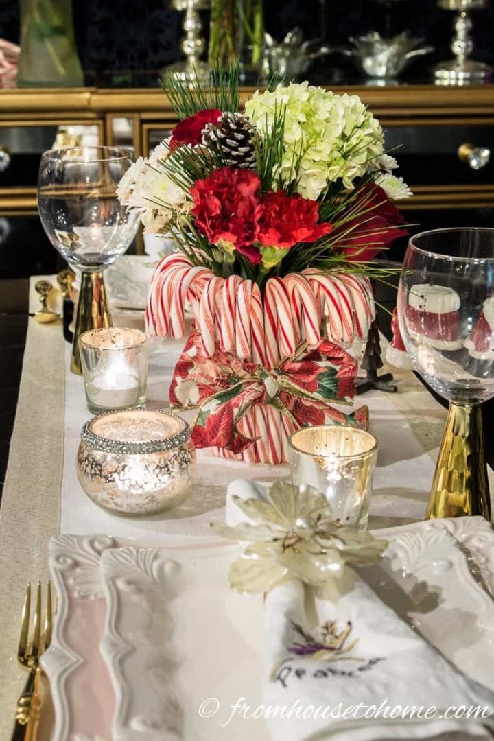 A red and white Christmas centerpiece made with candy canes and red and white flowers on a small dining table