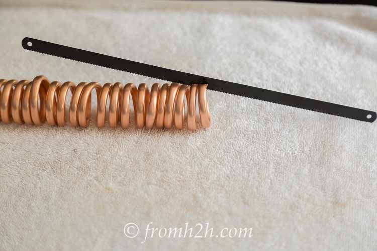Coiled copper tubing being cut into chain links using a hack saw