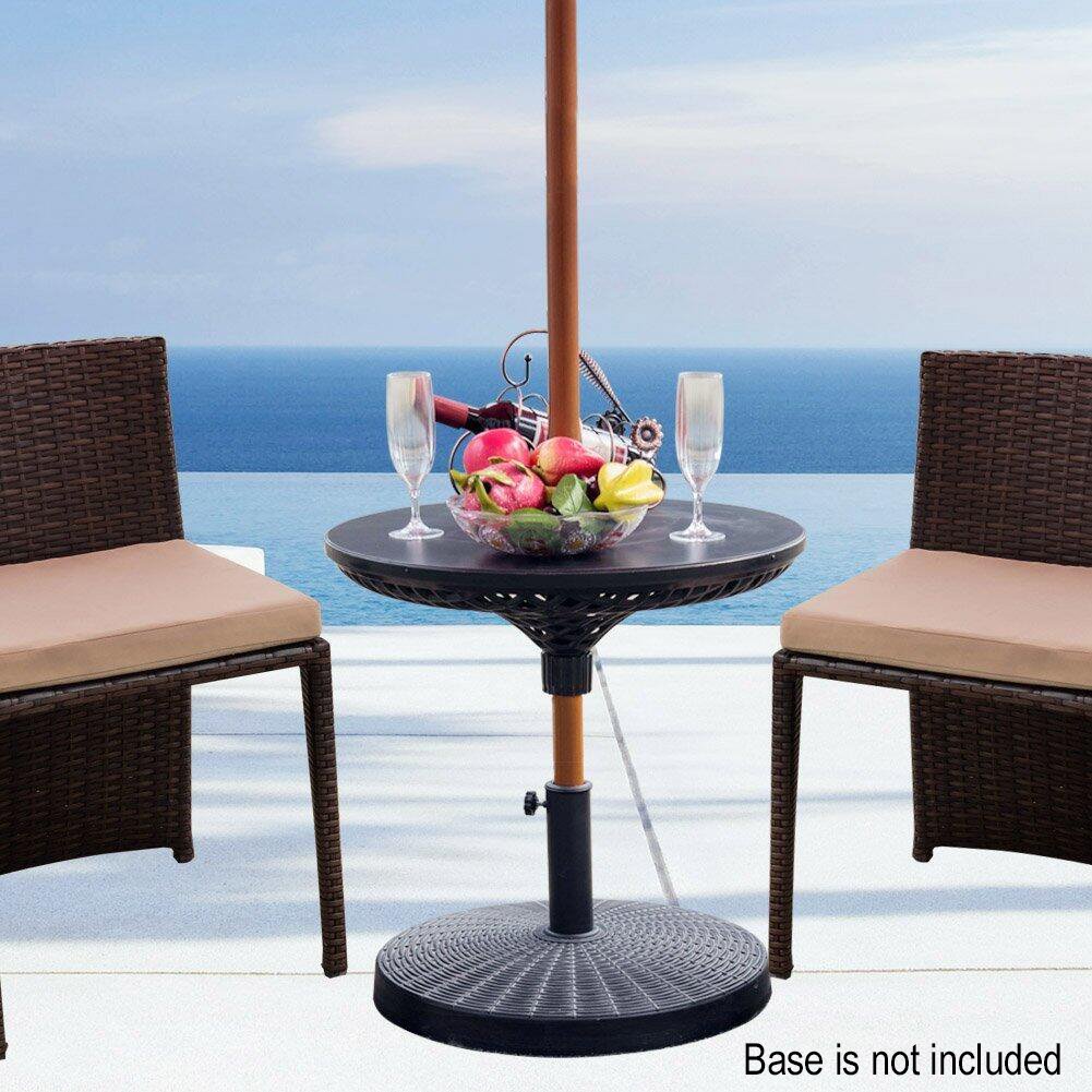 An umbrella table on an umbrella pole with a bowl of fruit and two glasses