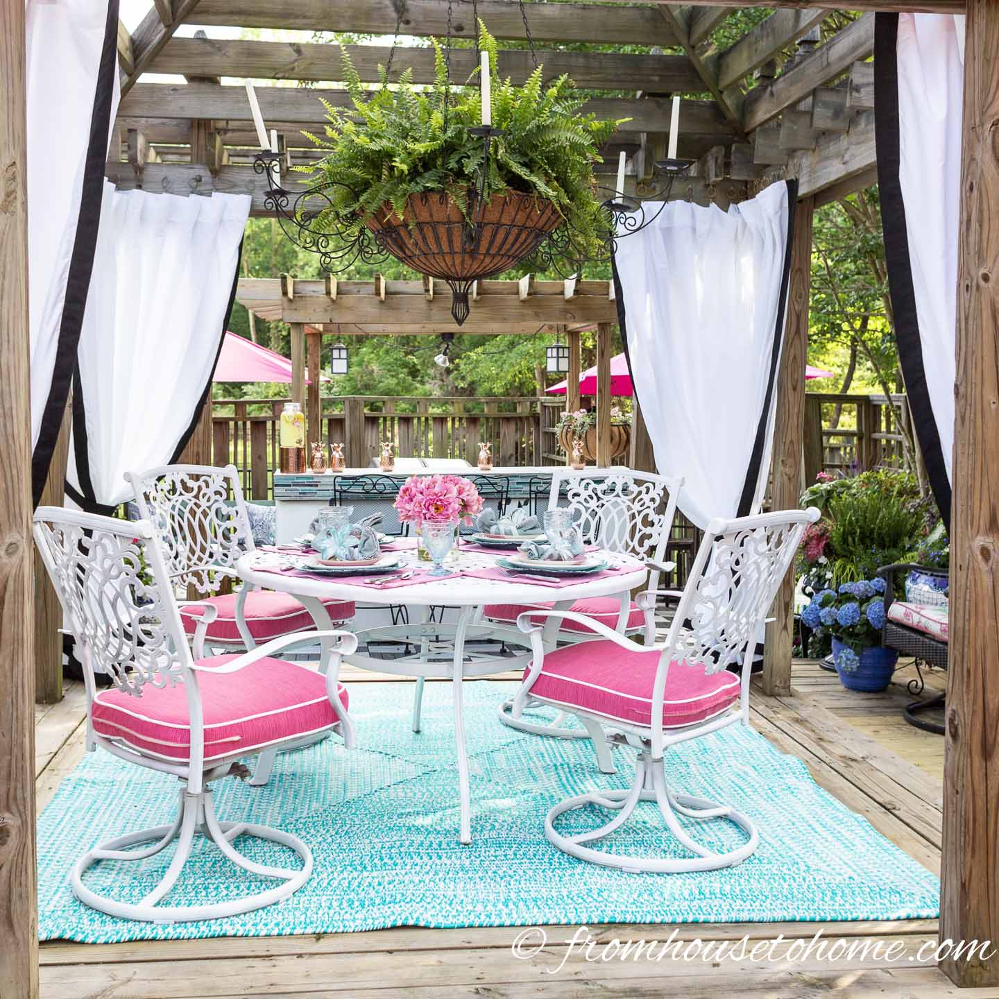 An outdoor dining table under a pergola with white curtains in each of the curtains