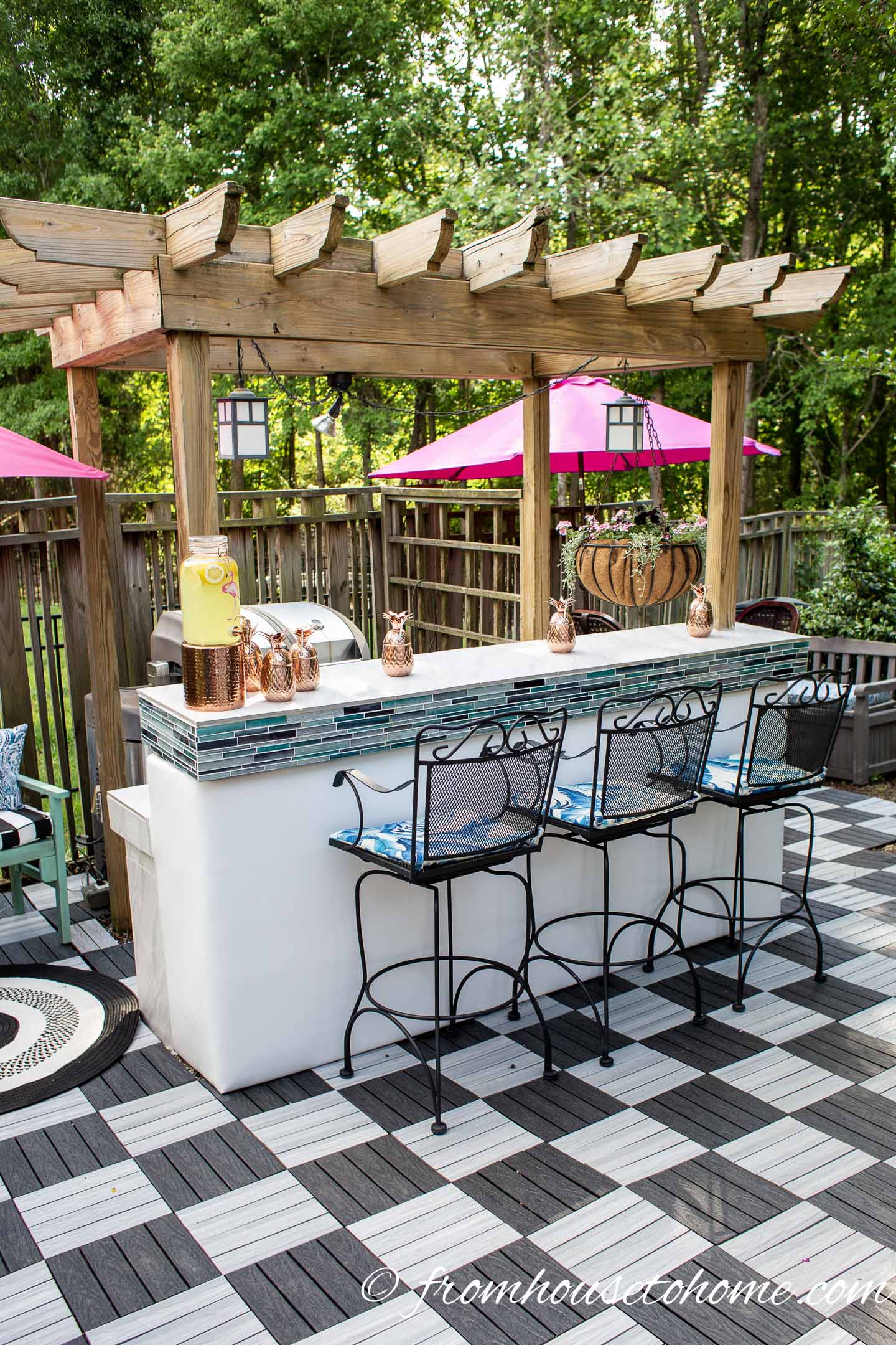 Pergola over an outdoor bar and grill area with 3 barstools and a black and white checkered patio
