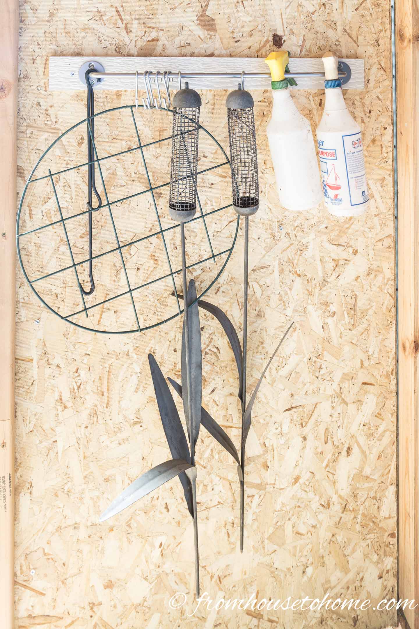 Bird feeders, spray bottles and flower cages hanging from a kitchen rod in a shed