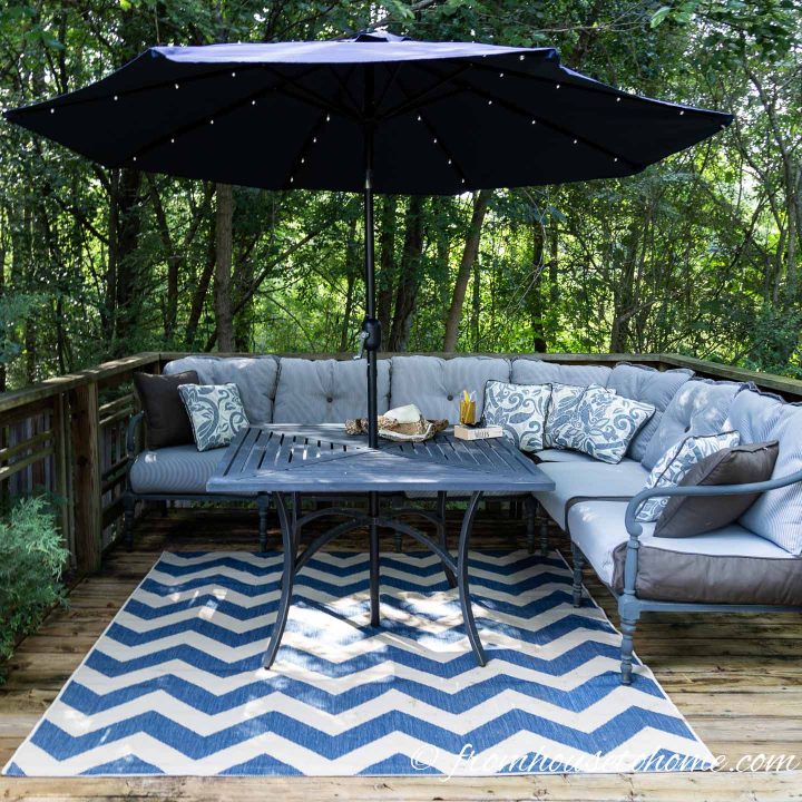 Deck decorated with a blue and white area rug, blue and white cushions and a blue umbrella