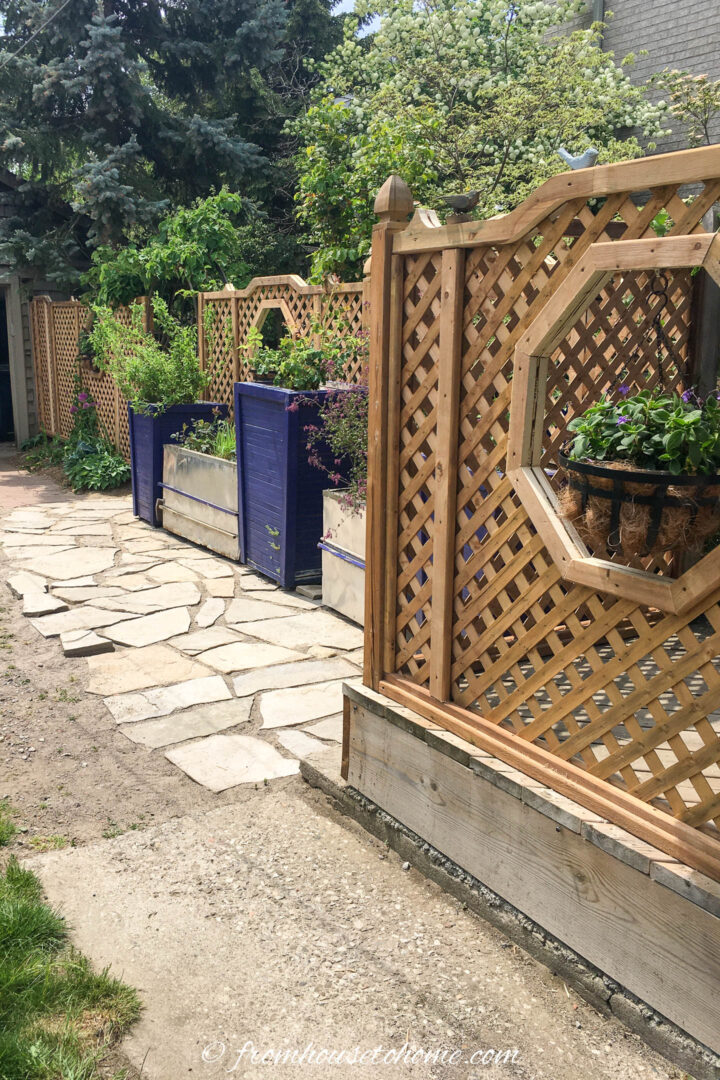 A fence beside a driveway with large containers full of plants