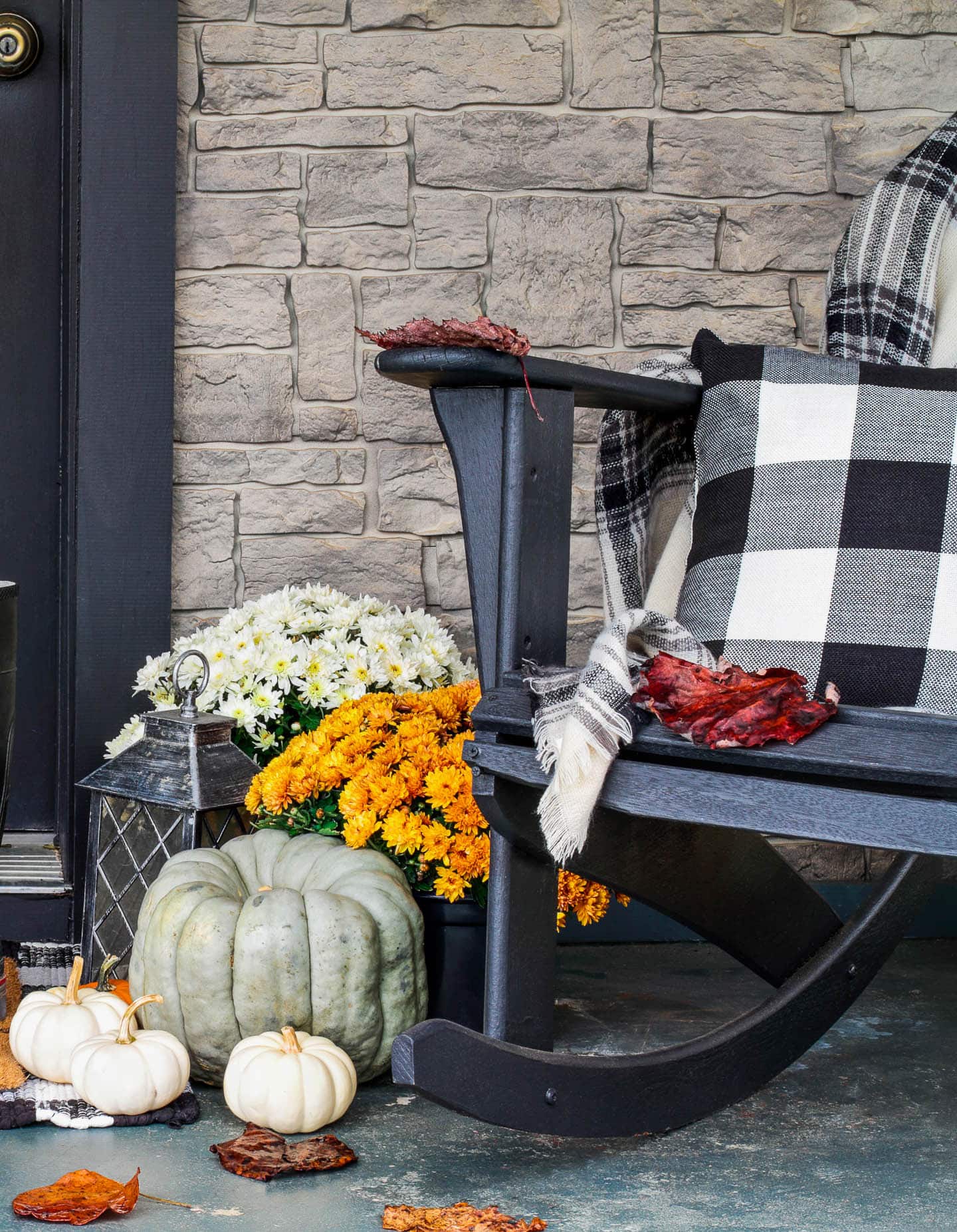 Front porch with a black and white outdoor rocker, white and orange mums, blue and white pumpkins and a black lantern