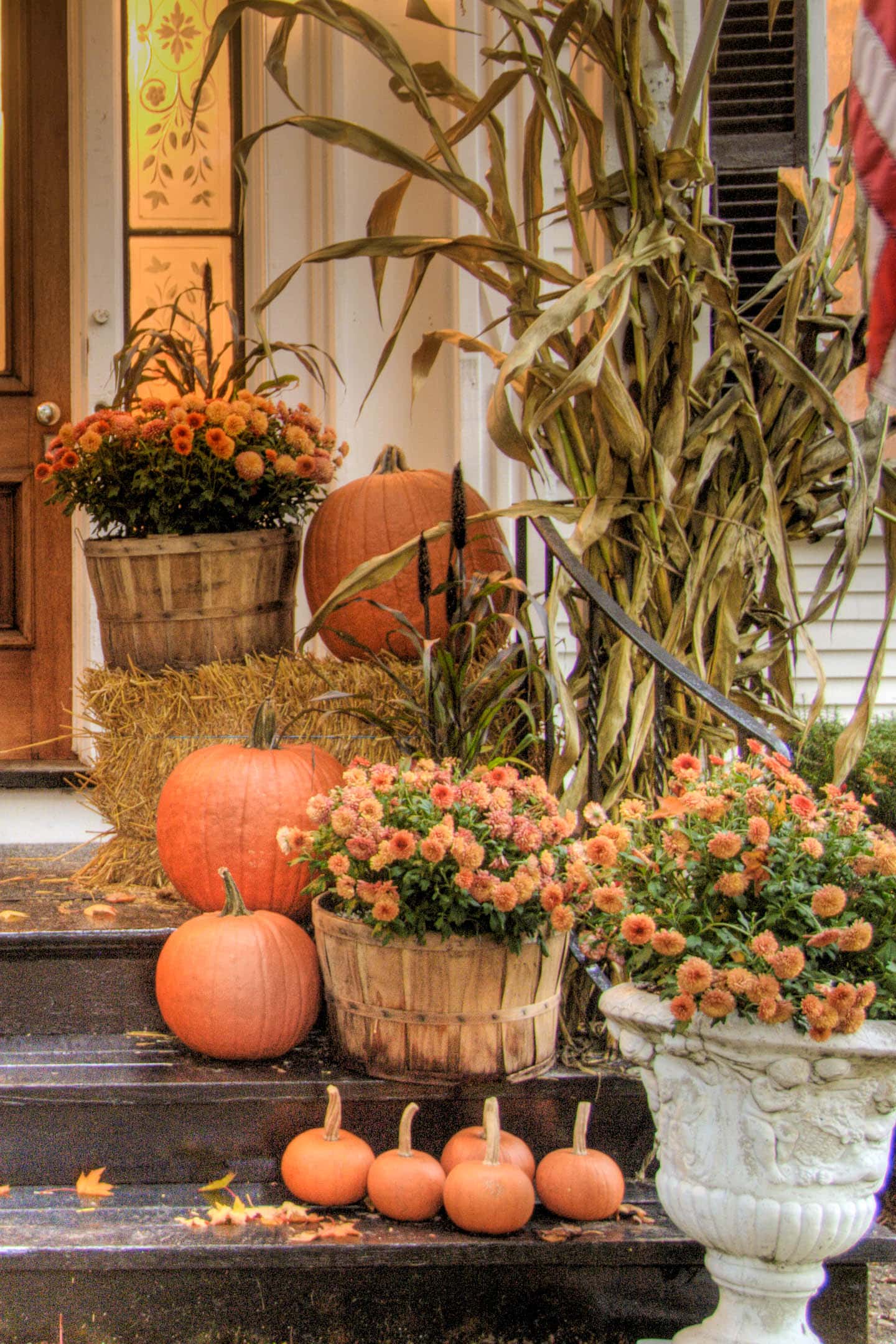 Orange Chrysanthemums, pumpkins, a bale of hay and a dried cornstalk on the front porch steps