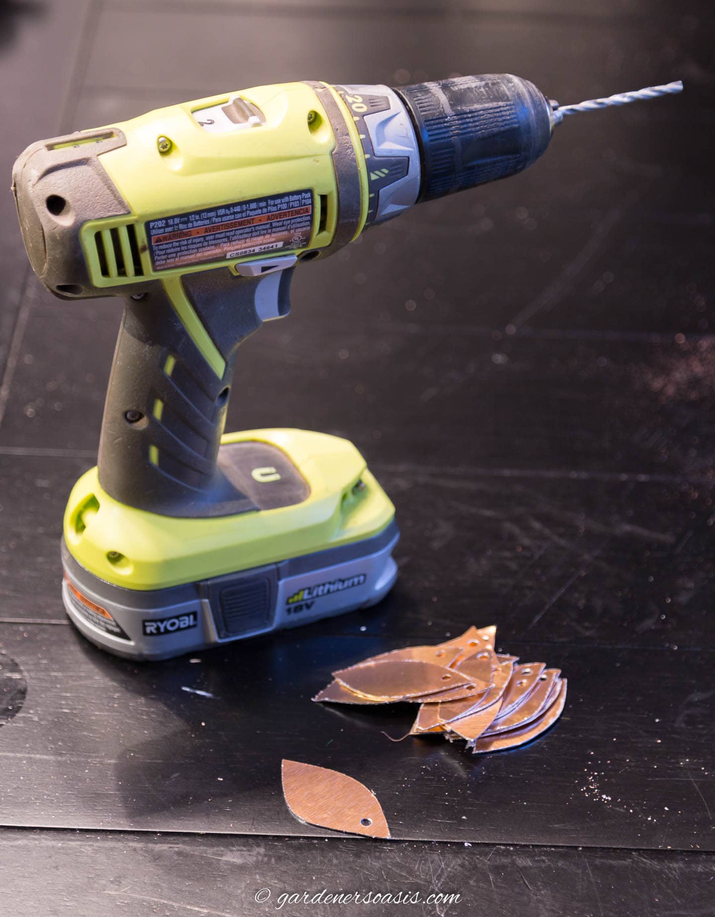 A pile of copper leaves with holes drilled in the top beside a cordless drill