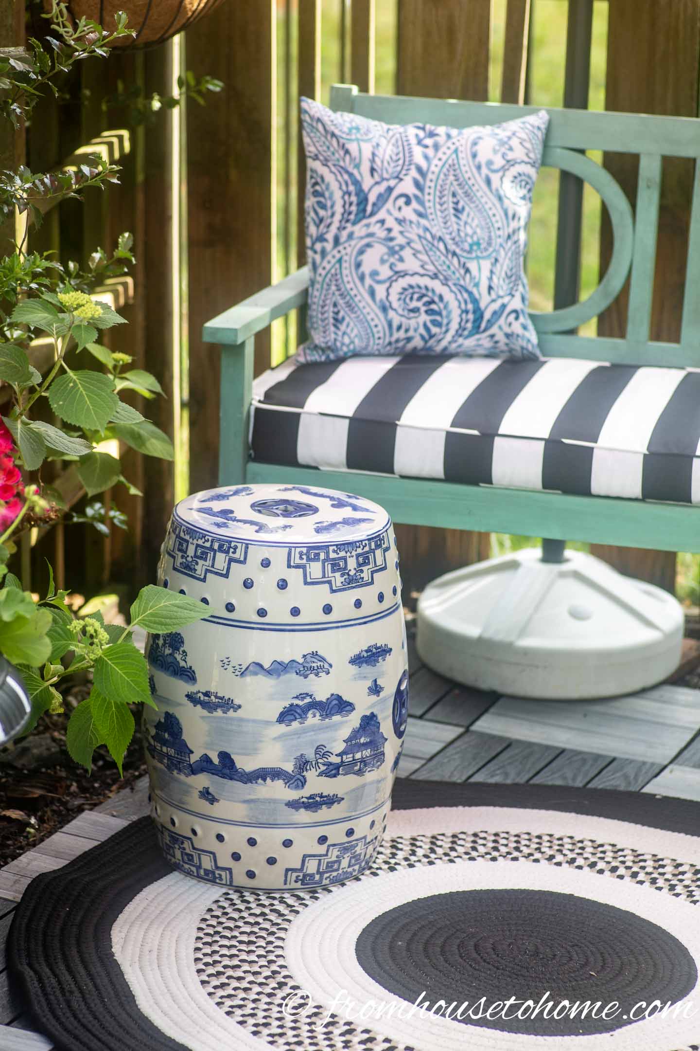 A blue and white garden stool being used as a side table beside a bench on a small patio