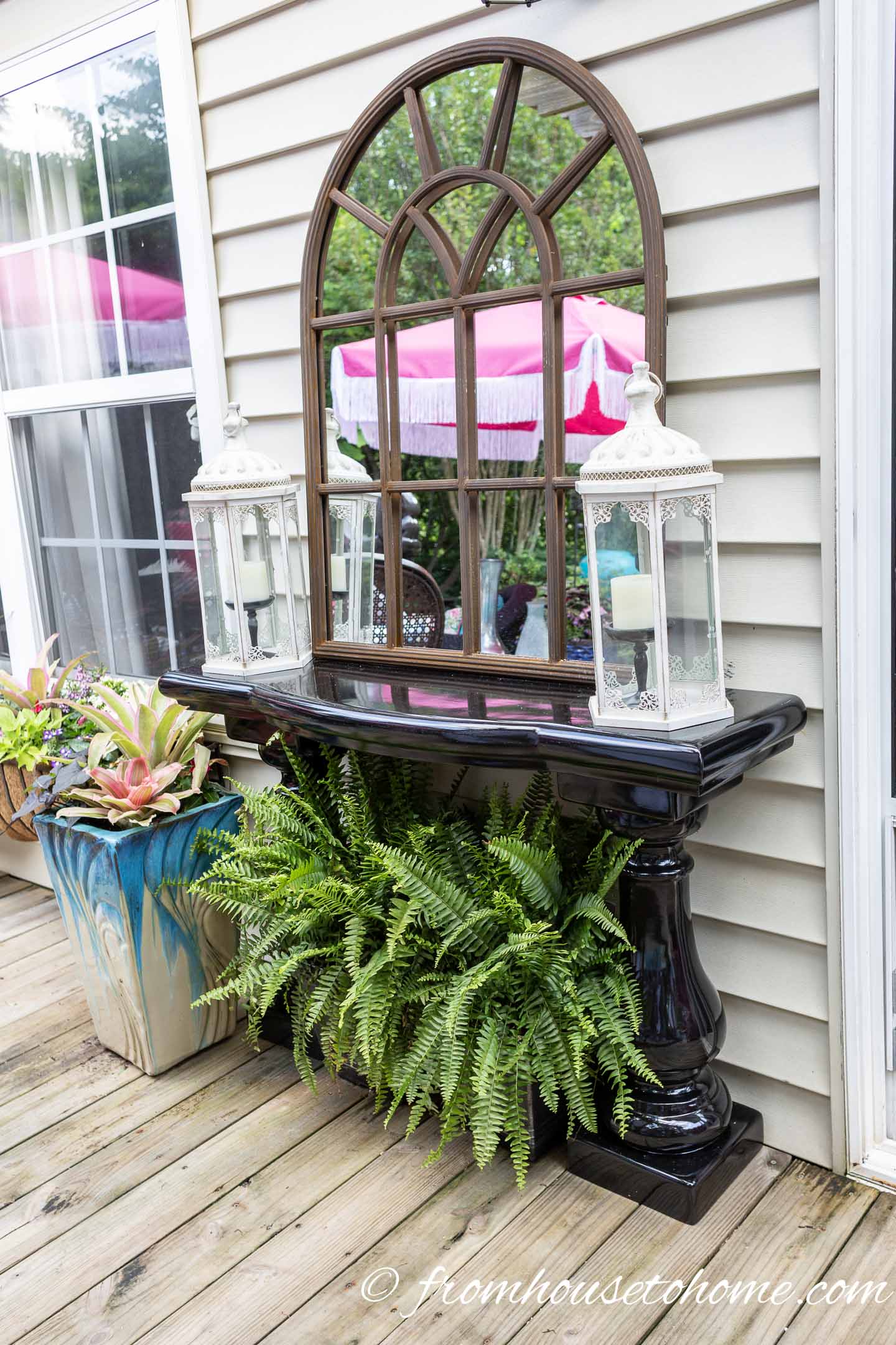A garden mirror on an outdoor console table at the edge of a small deck