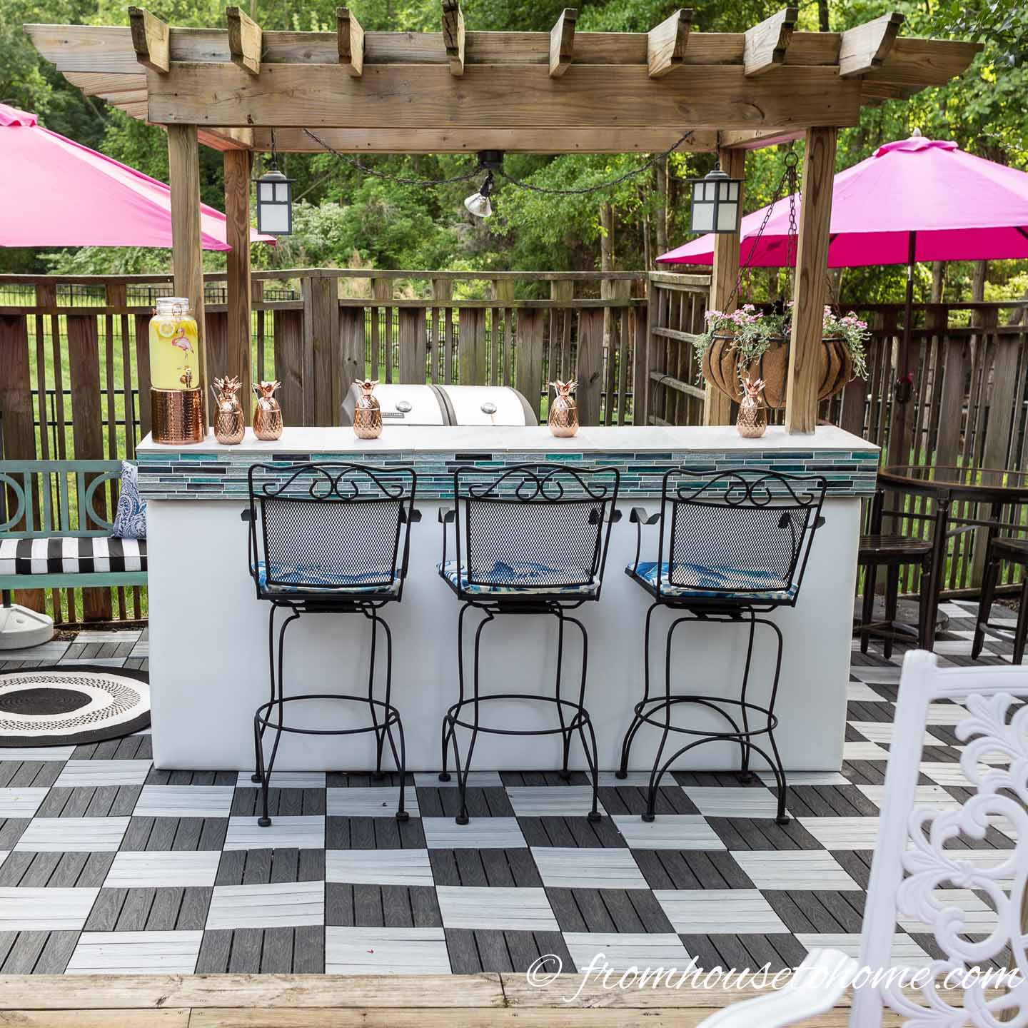 An outdoor bar with 3 tall chairs on a black and white checkered outdoor patio