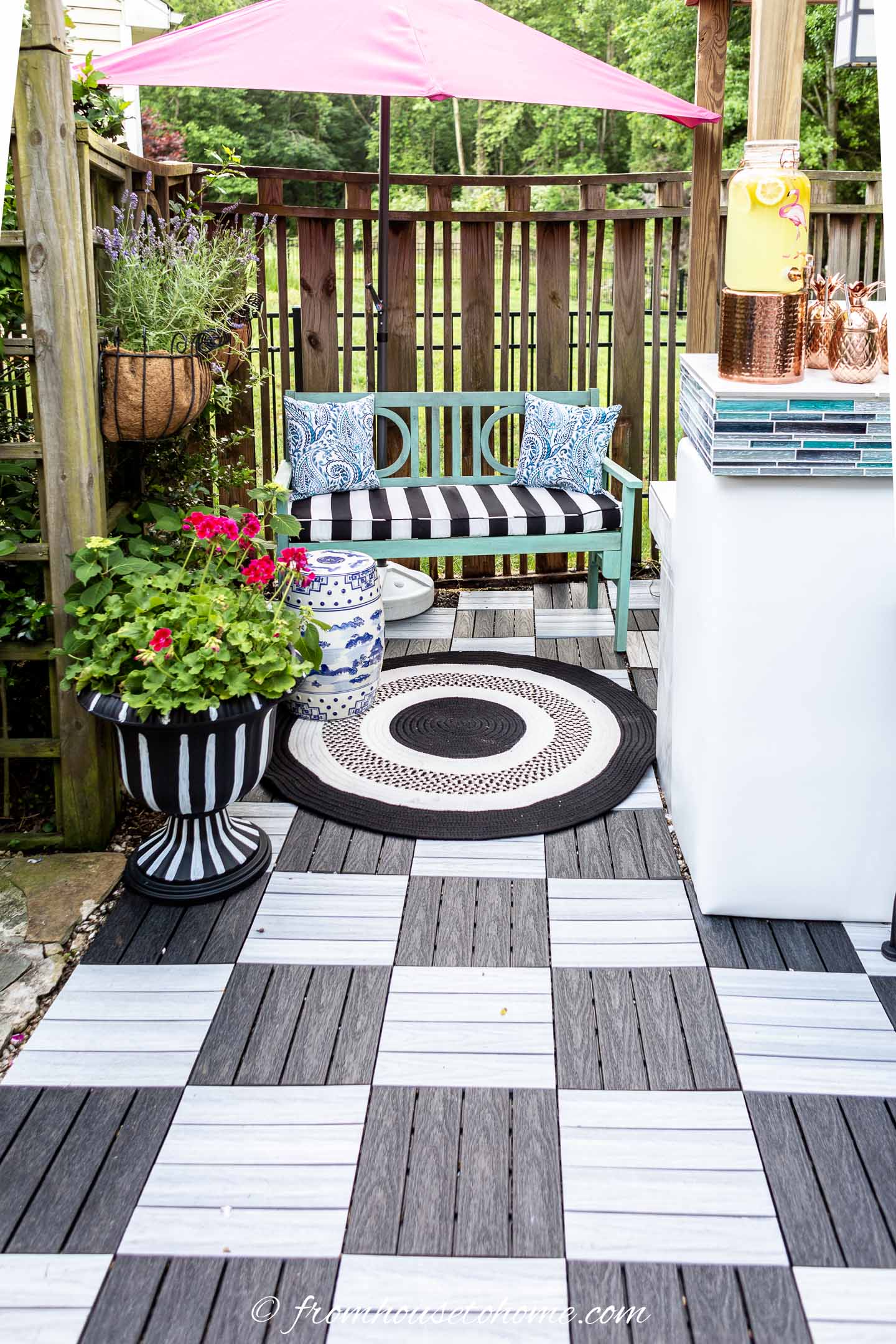 A turquoise bench and round black and white rug on a small patio made of black and white deck tiles