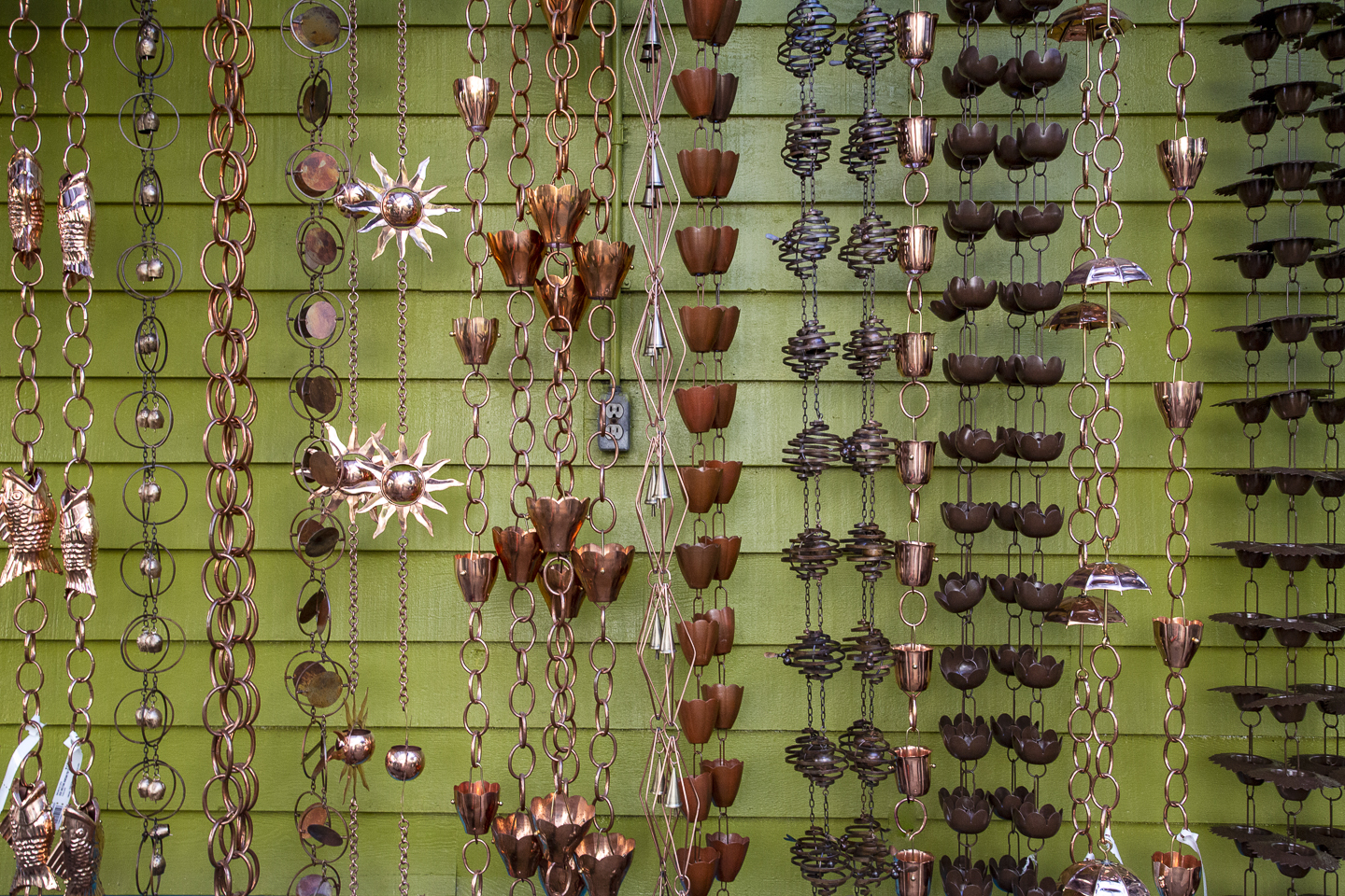 Many different types of rain chains hanging in front of a wall