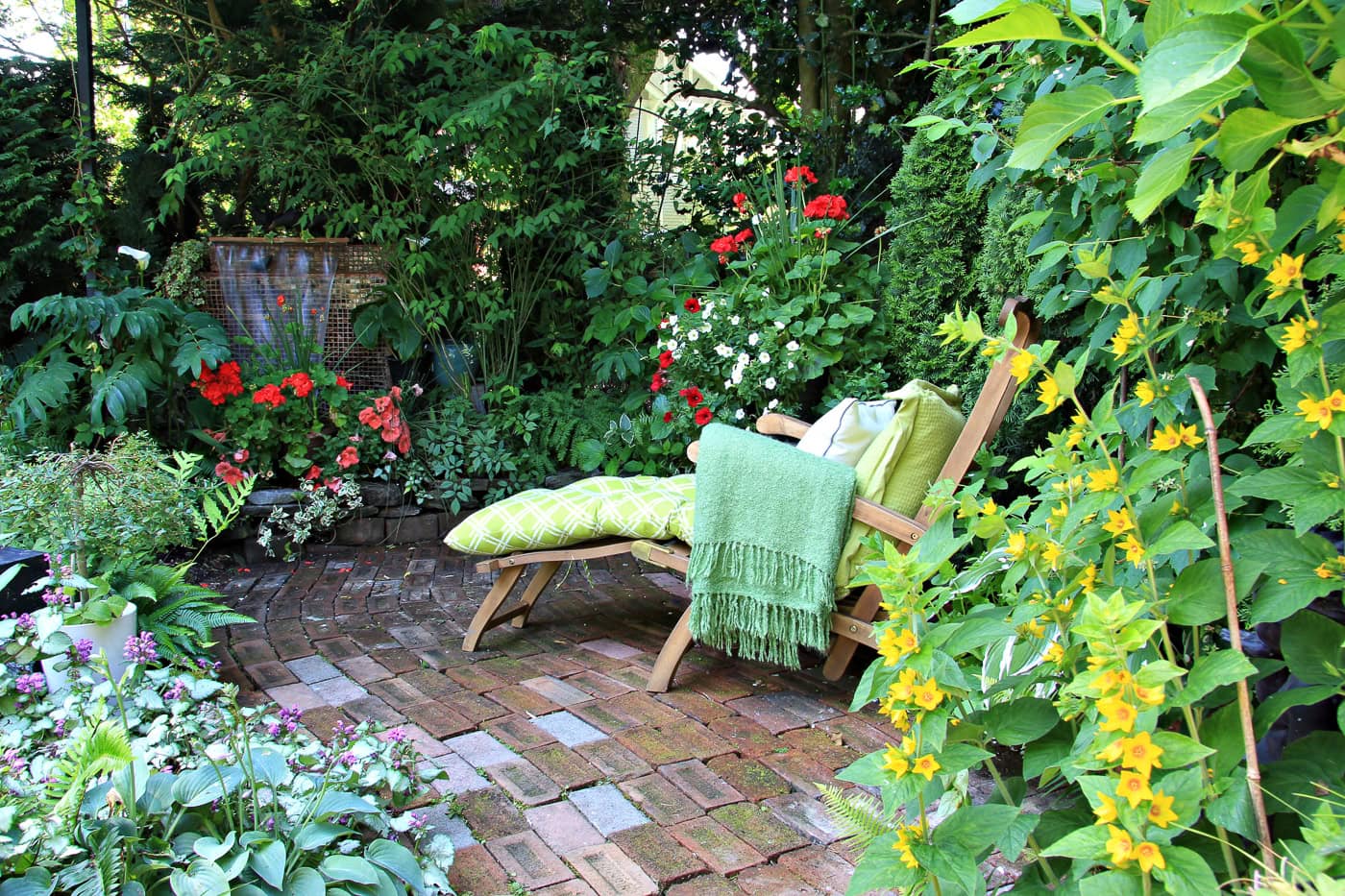 Comfortable lounge chair on a small private patio with a water fountain lots of plants around it