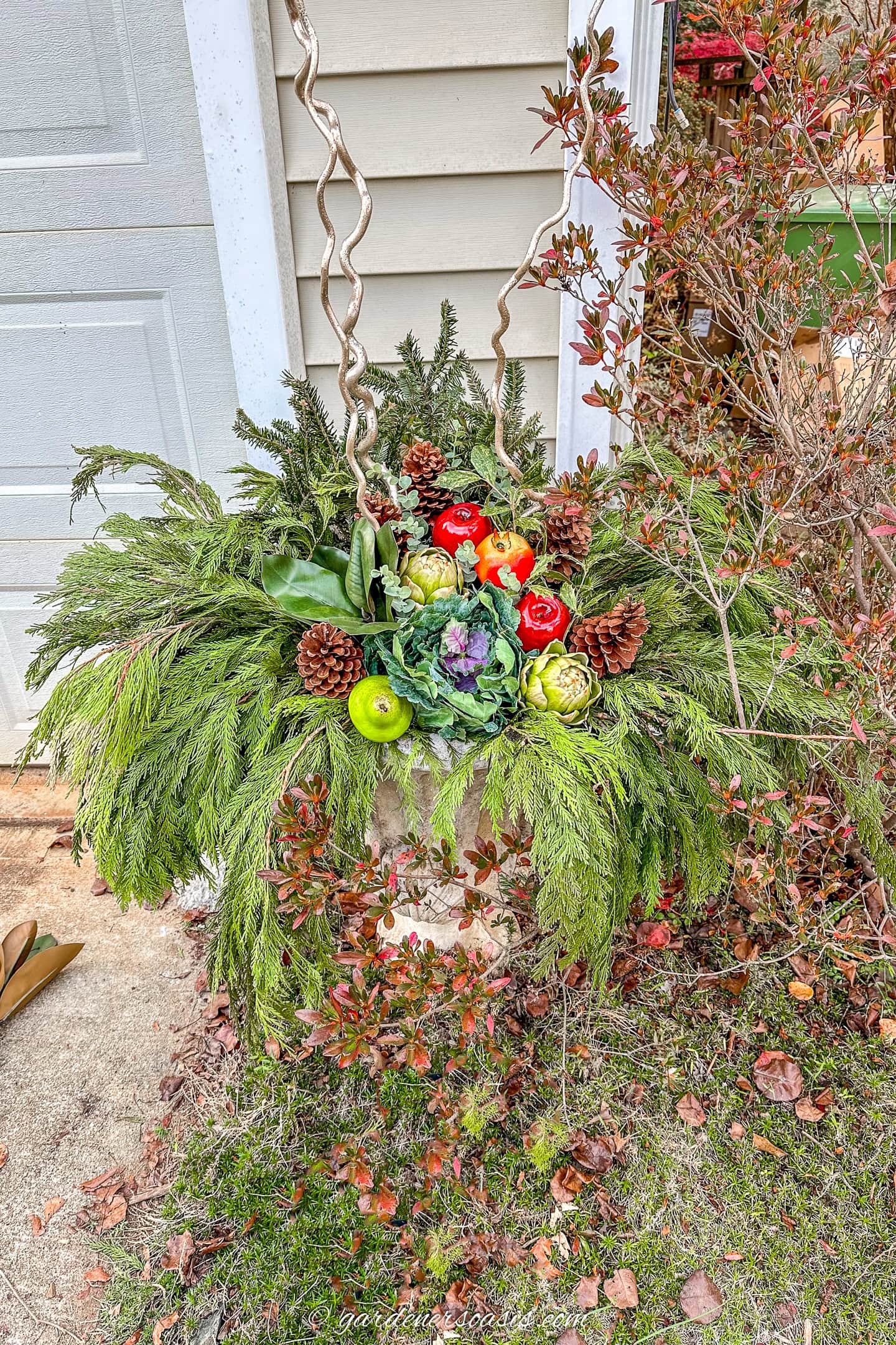 diy urn winter planter with cedar, spruce, magnolia leaves, faux fruit, faux kale, holly, eucalyptus picks and curly willow branches