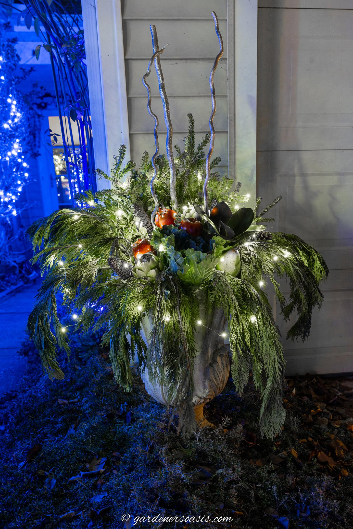 a lighted diy urn winter planter with evergreens and artificial greens and fruit
