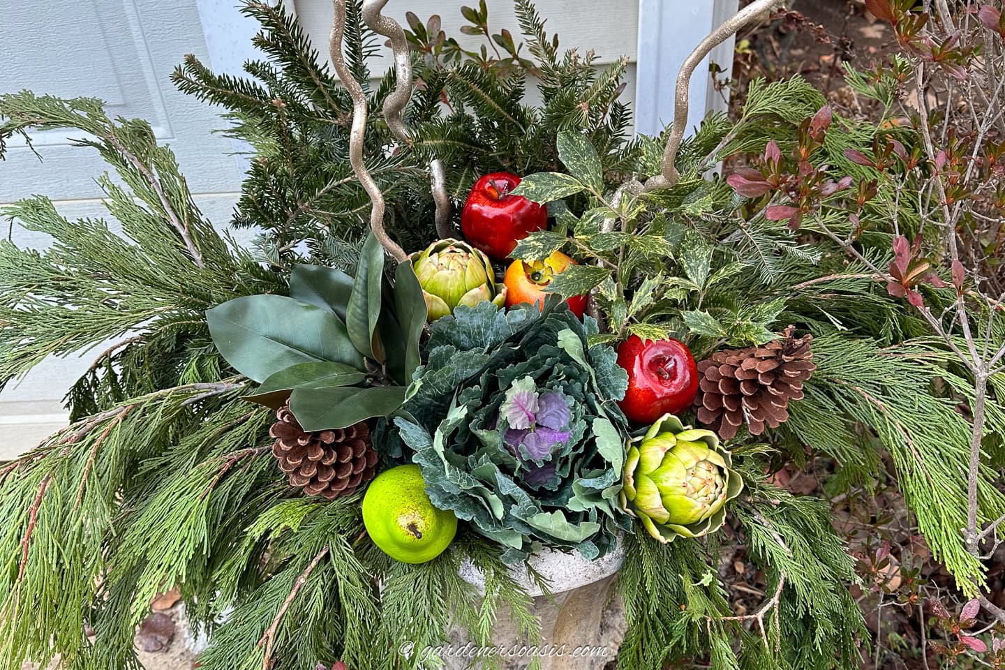 pinecones and aritificial fruit in a DIY urn winter planter with cedar, spruce, magnolia leaves, holly and curly willow branches