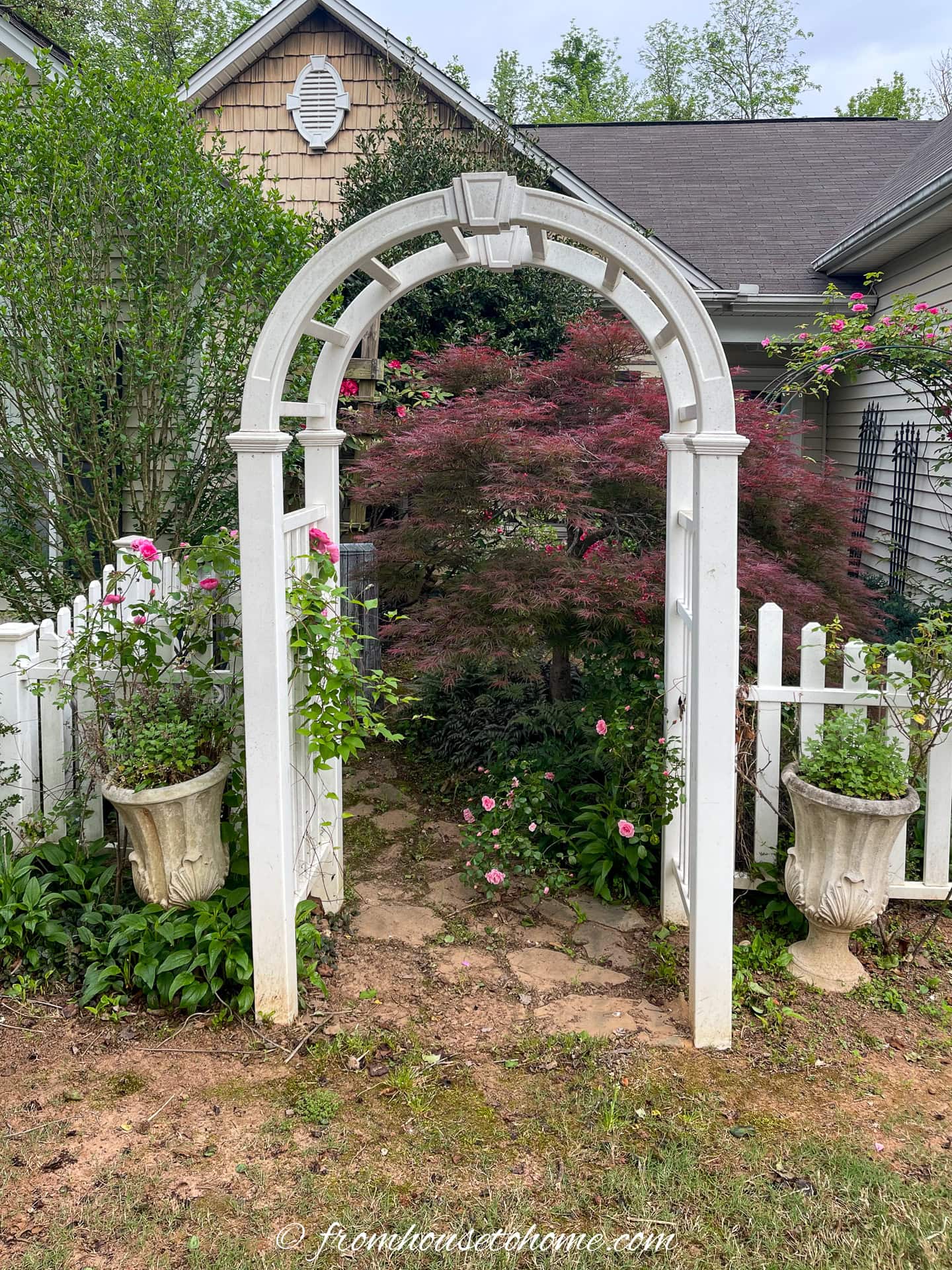 A white arbor and picket fence in a front yard designed like a Charleston courtyard