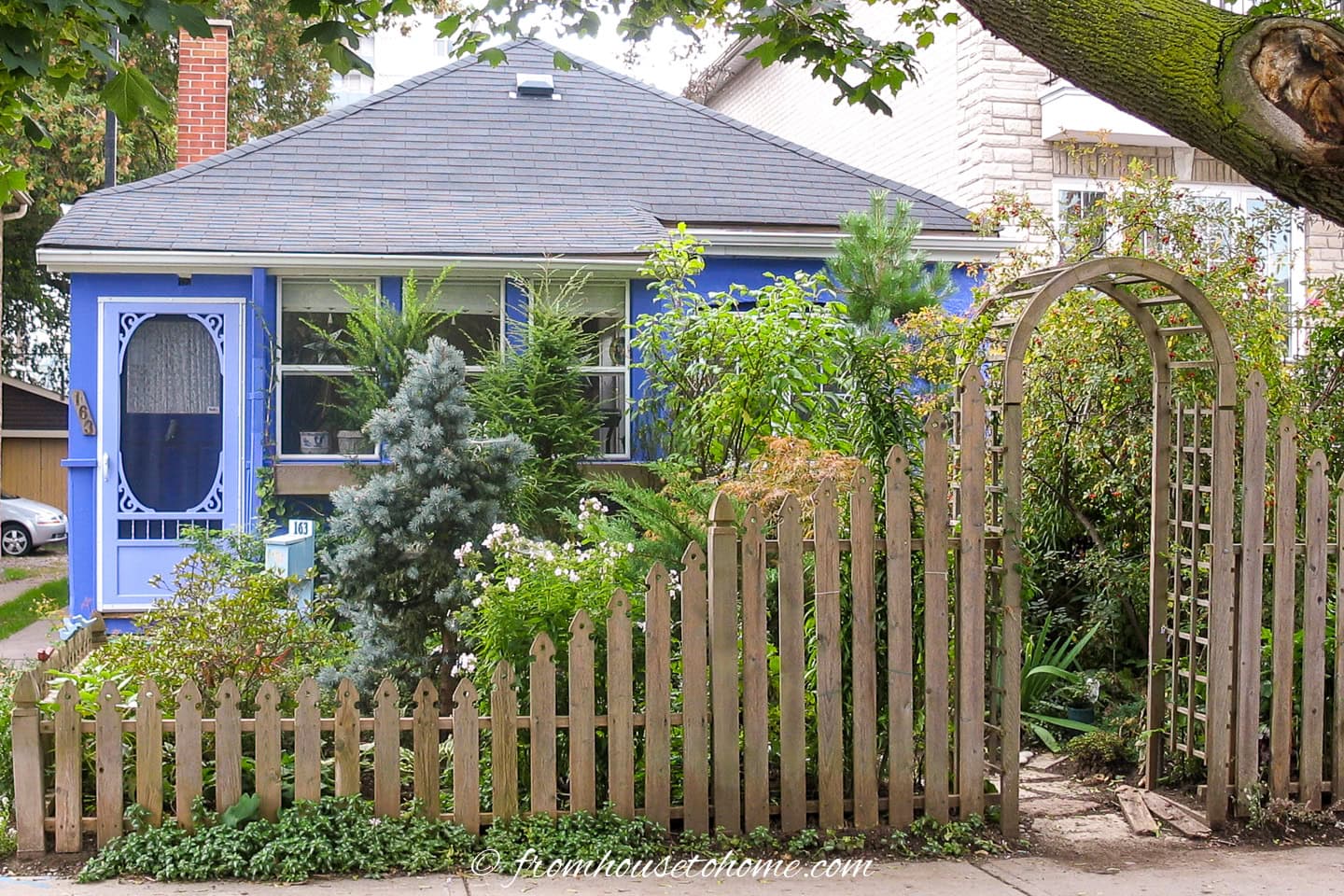A cottage garden with a picket fence and arbor in a small front yard