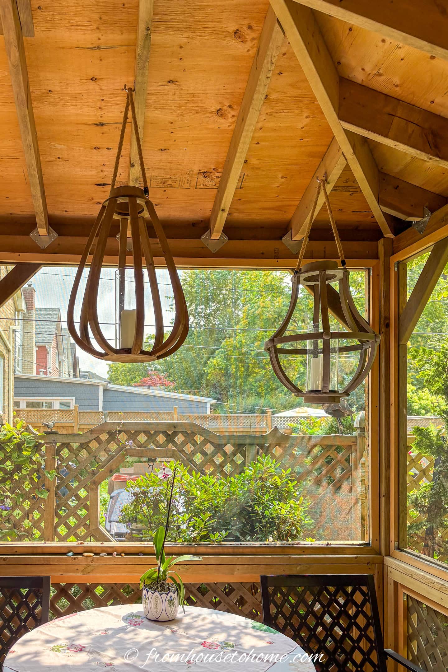 Two wooden hanging lanterns above a dining table in a gazebo