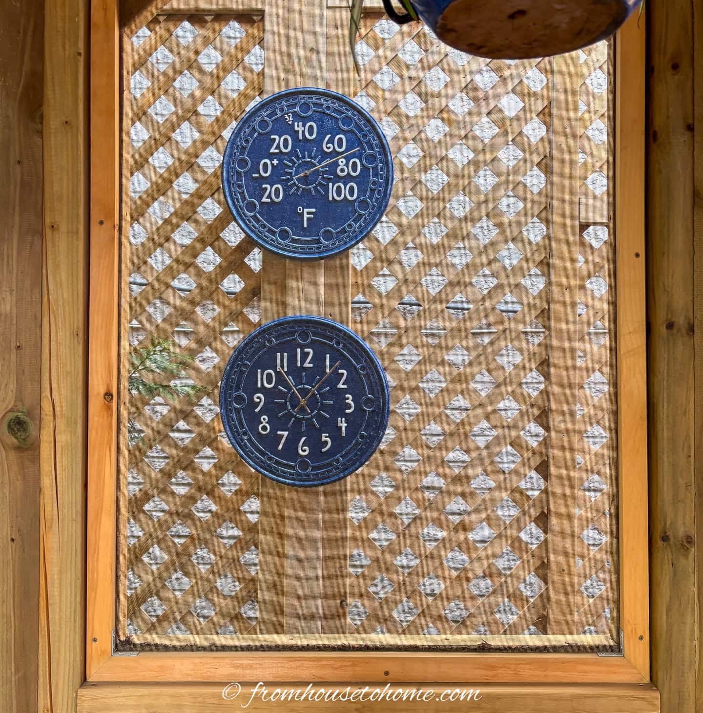 Two round dials hang on a wooden lattice wall; the top shows temperature in Fahrenheit, the bottom shows the time as 1:22.