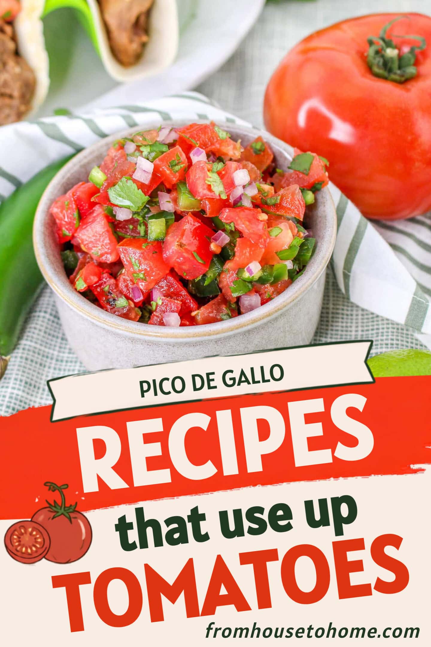 A bowl of fresh pico de gallo with diced tomatoes, onions, and jalapeƱos sits on a striped cloth next to a whole tomato, jalapeƱo, and lime. Tacos are partially visible in the background.