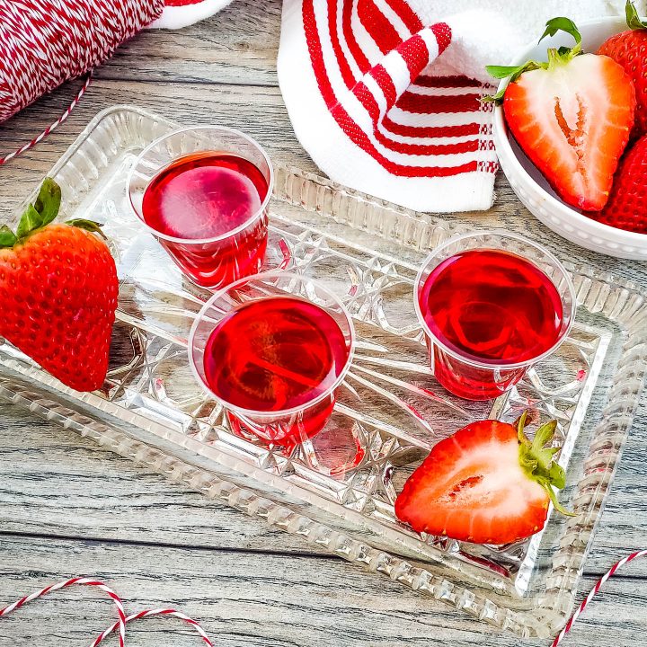 apple strawberry jello shots on a clear tray with strawberries