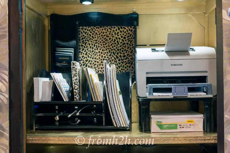 Top shelf of a TV armoire desk with a paper holder, charging station, printer and bulletin board