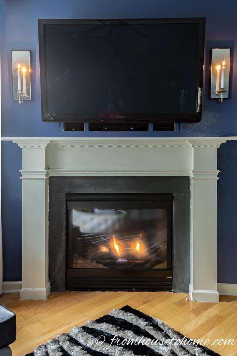 A lit fireplace with the DIY traditional fireplace mantel painted white and a TV above it