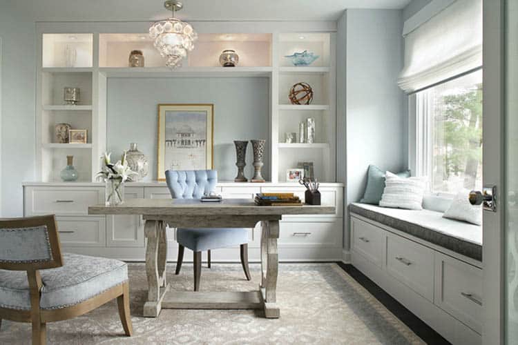 Light blue office with a chandelier and a grey desk by the window with a window seat