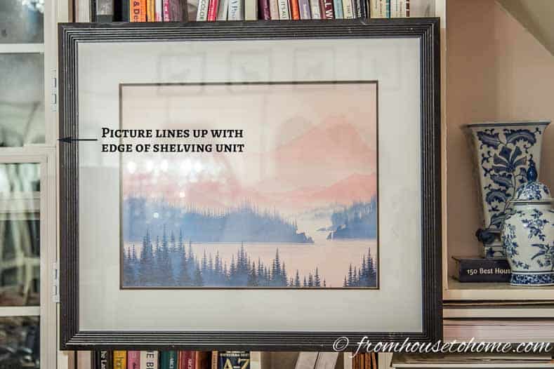 The picture needs to line up with either an upright or a shelf | How To Hang Art On A Bookcase (And Still Have Easy Access To The Books)