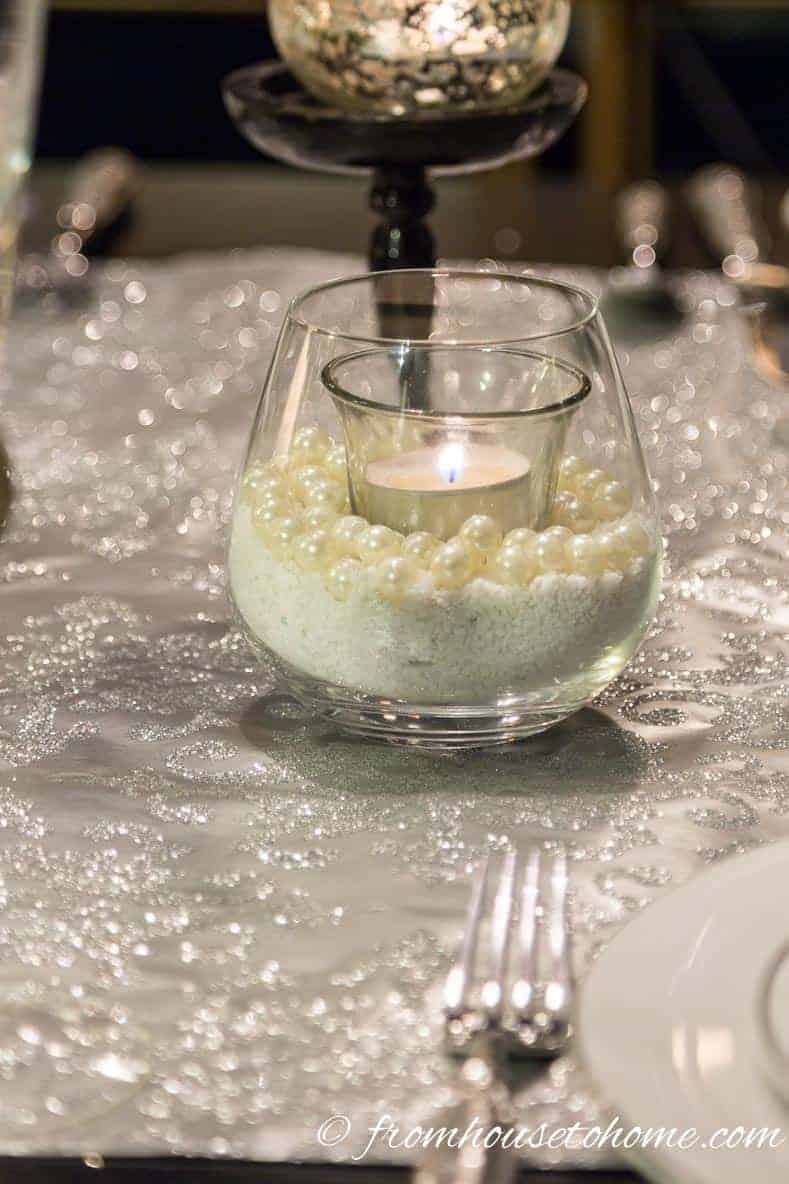 A stemless wine glass with sand and faux pearls used as a candle holder