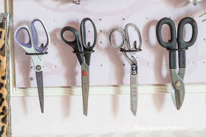 Sewing scissors and other craft room supplies hung on a pegboard with plier hooks