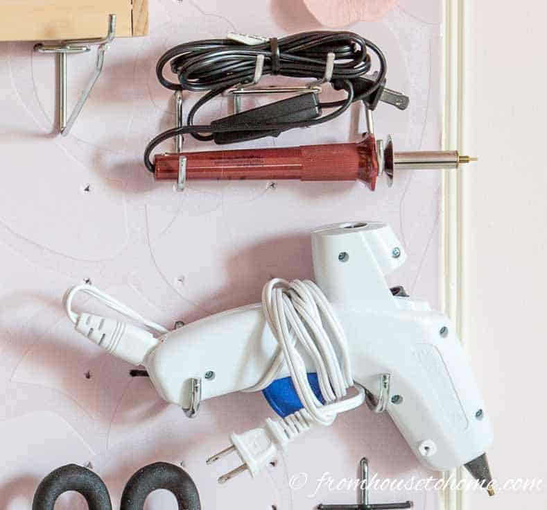 A glue gun and engraver hung on a pegboard wall in a craft room