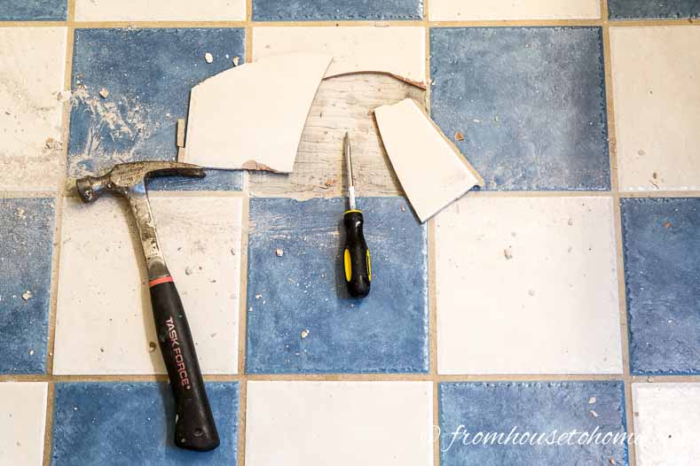 Half of a tile removed on a blue and white tiled floor with a hammer and screw driver