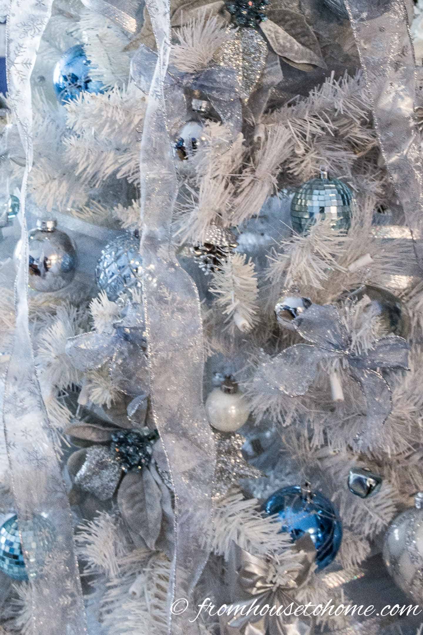Silver ribbons with light blue ornaments on a white Christmas tree