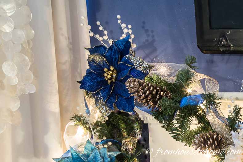 Blue poinsettia ornament on the garland with white pearl picks behind it