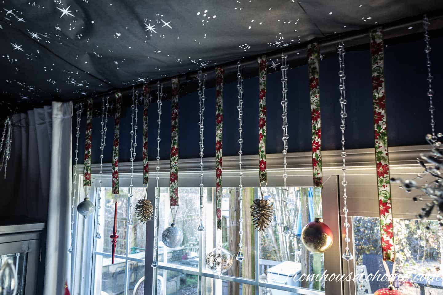 Red, white and gold Christmas ornaments hung with ribbons from a curtain rod in front of a window