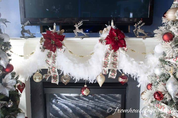 Poinsettias and white feather boas used as Christmas decorations on a fireplace mantel under a TV