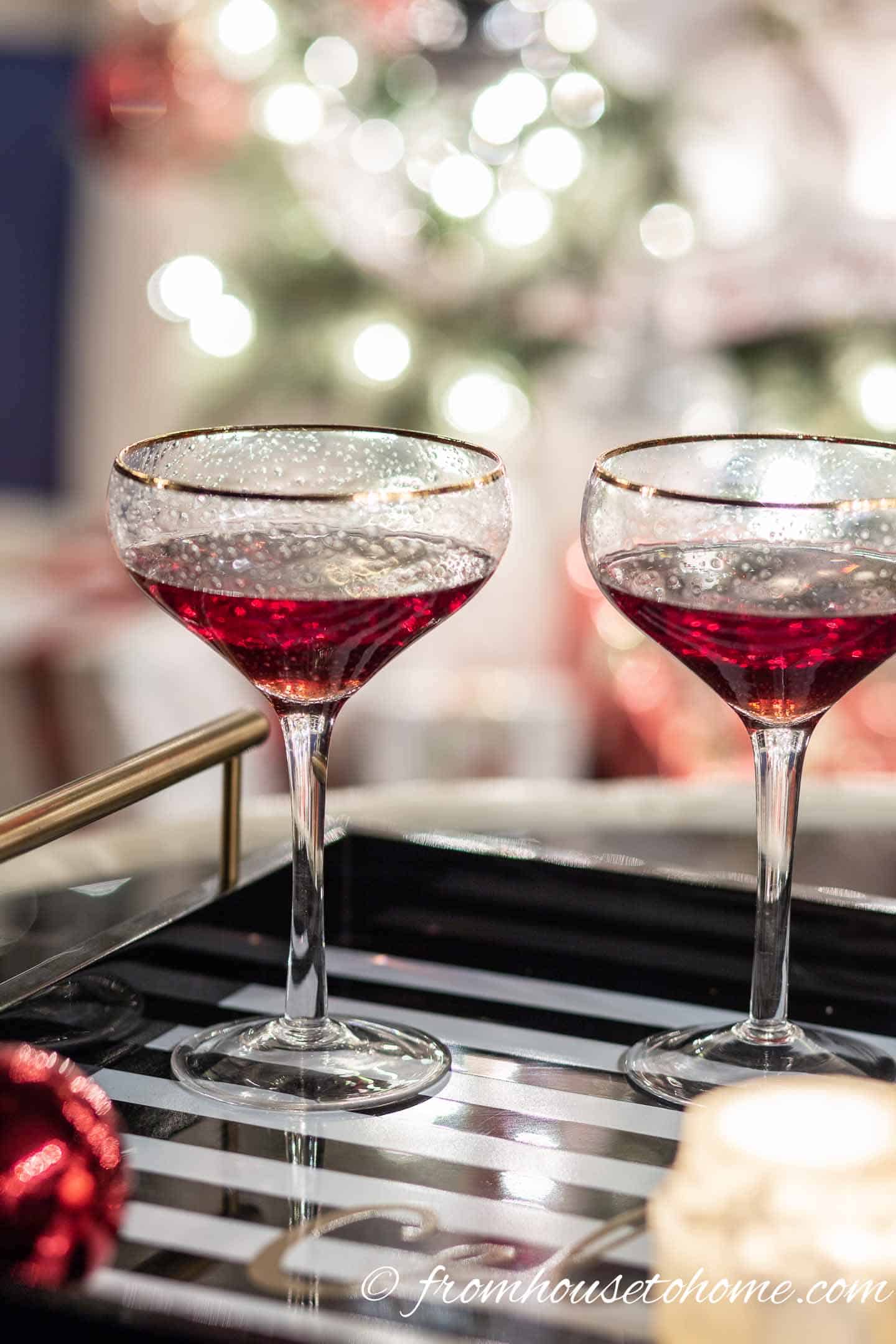 Two cranberry martinis on a table in front of Christmas lights