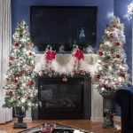 white and red Christmas trees on either side of a fireplace mantel with a TV above it