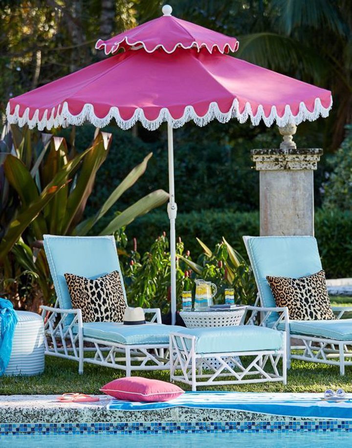 Pink patio umbrella with white fringe over turquoise chaise lounges