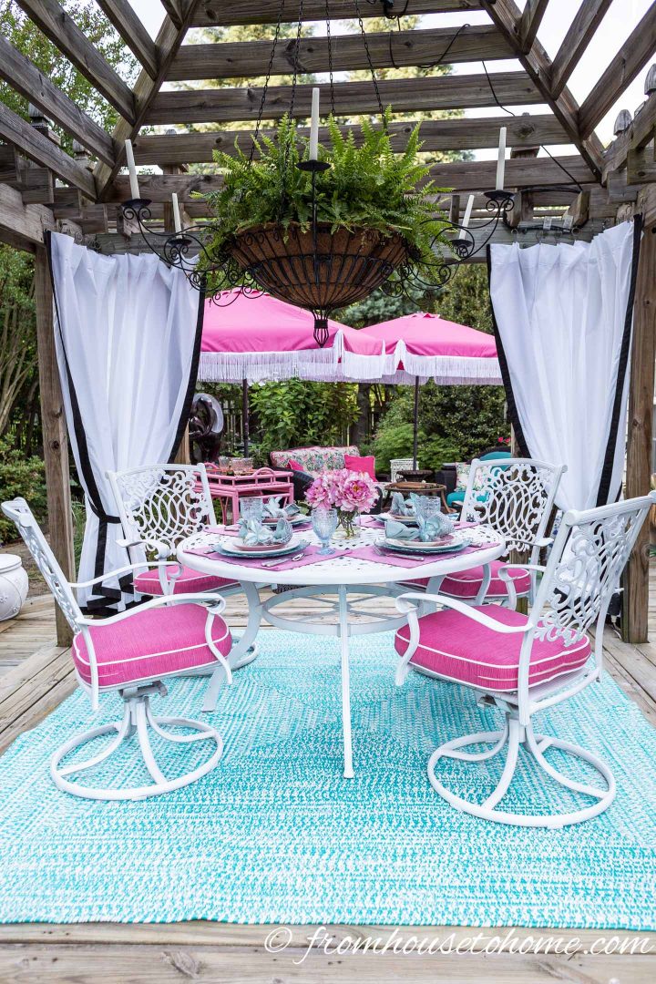 Outdoor patio furniture painted white in a gazebo with a large fern hanging in the center and white curtains in the corners