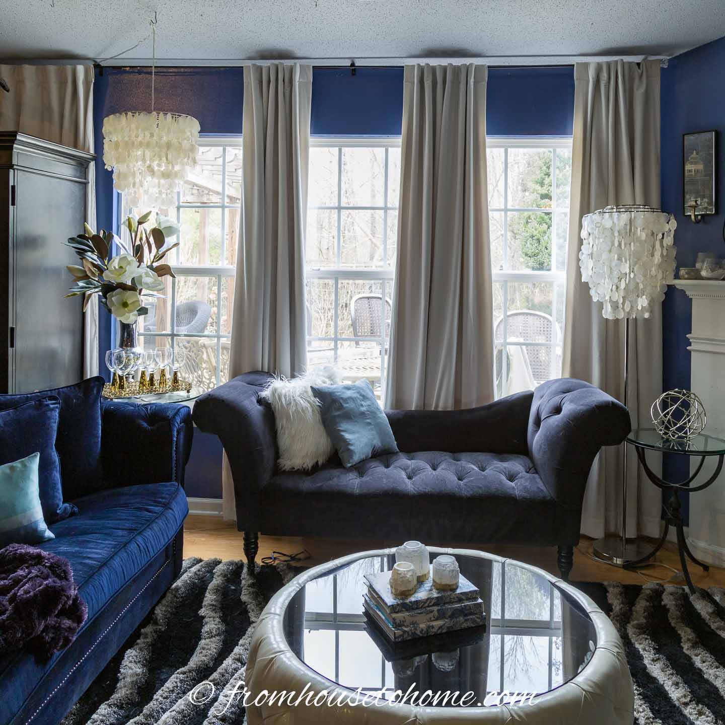 A living room with dark blue walls, white curtains and a black sofa