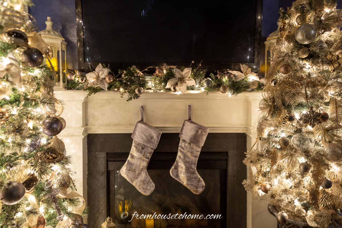 Fireplace mantel decorated for Christmas with stockings, a garland and 2 Christmas trees on either side