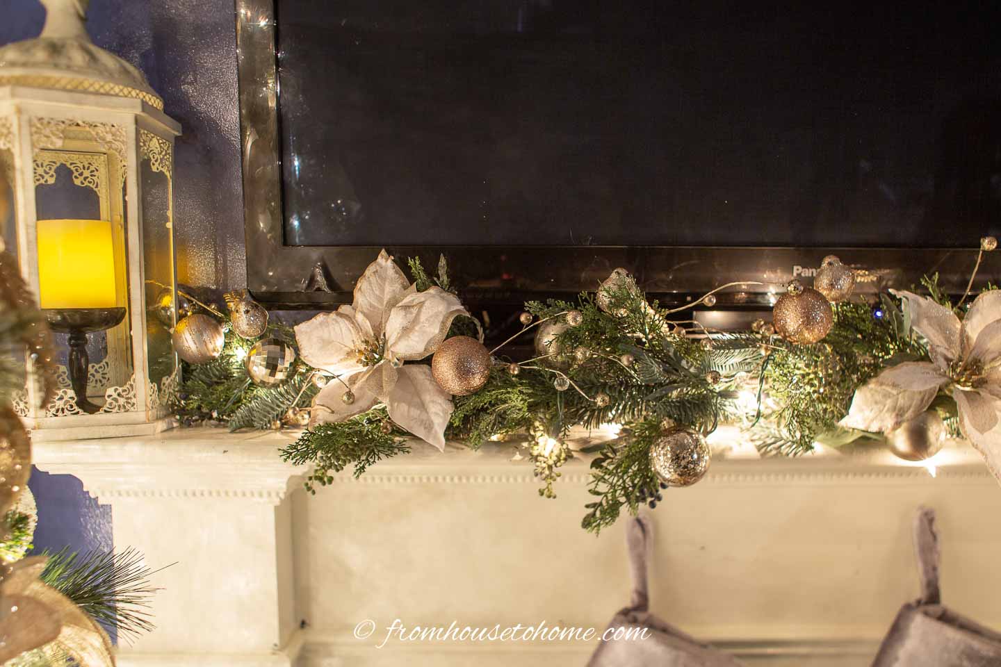 A Christmas garland on a mantel made with faux evergreens, white and gold poinsettias and copper and gold Christmas ornaments