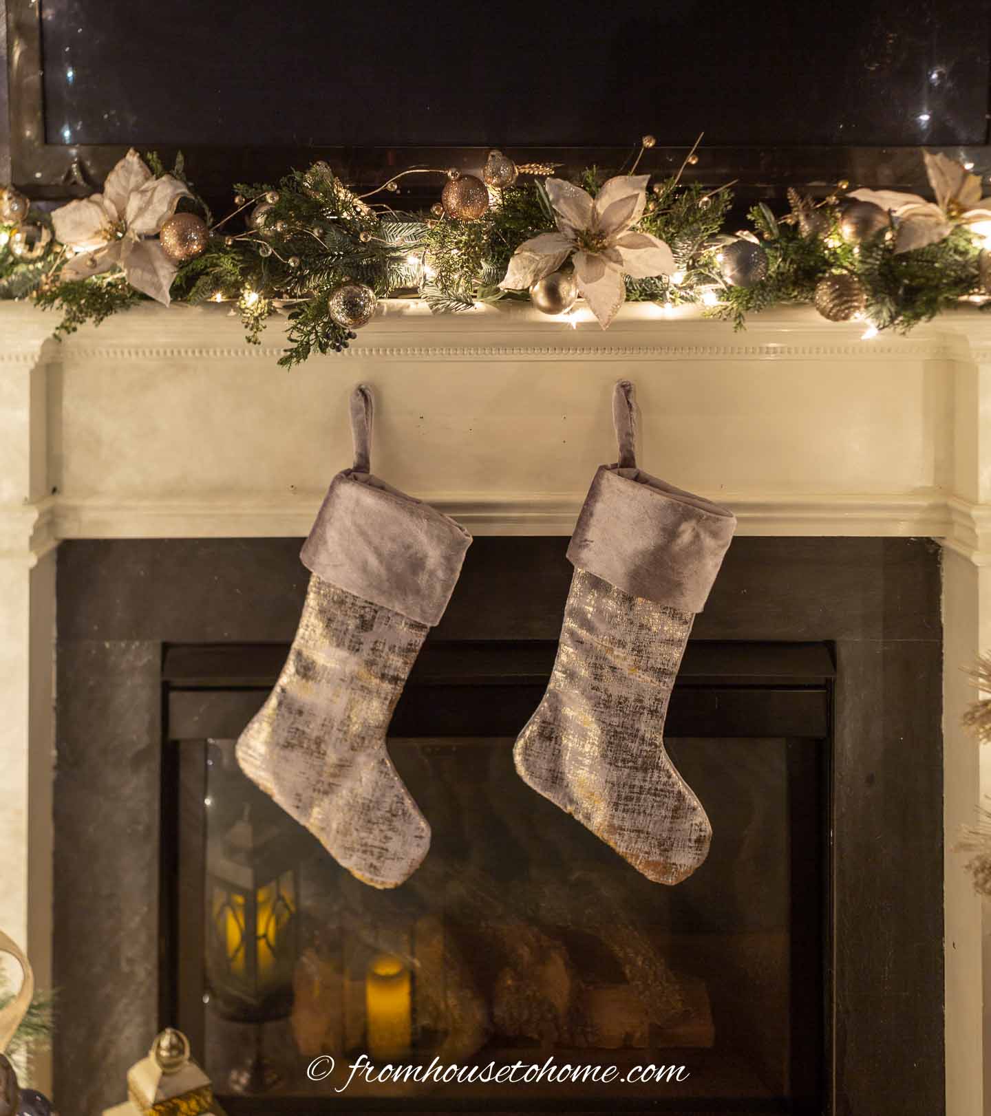 A fireplace mantel with a Christmas garland on top and 2 silver stockings hung on the front