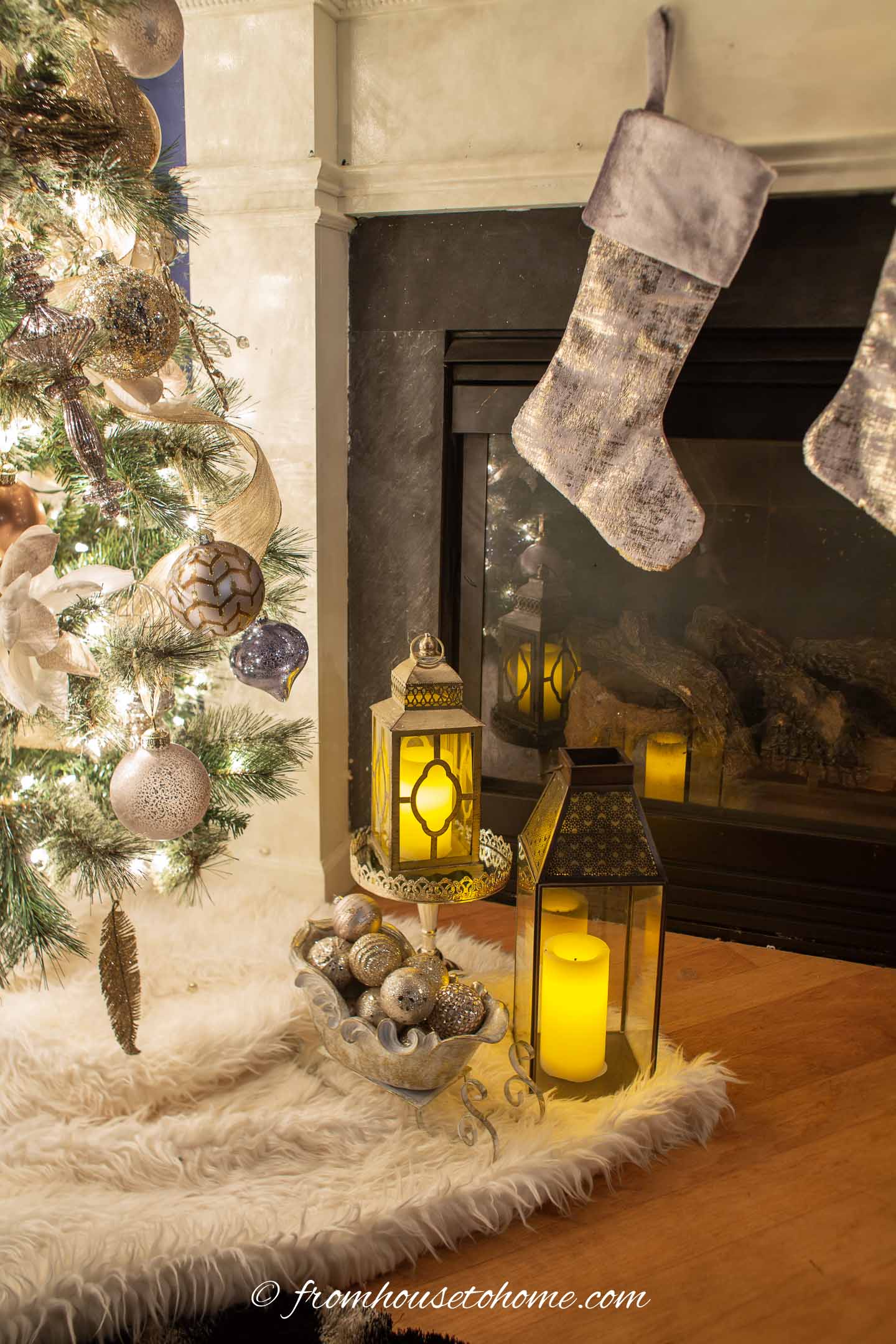 Two lanterns and a decorative sleigh filled with Christmas ornaments between the Christmas tree and the fireplace