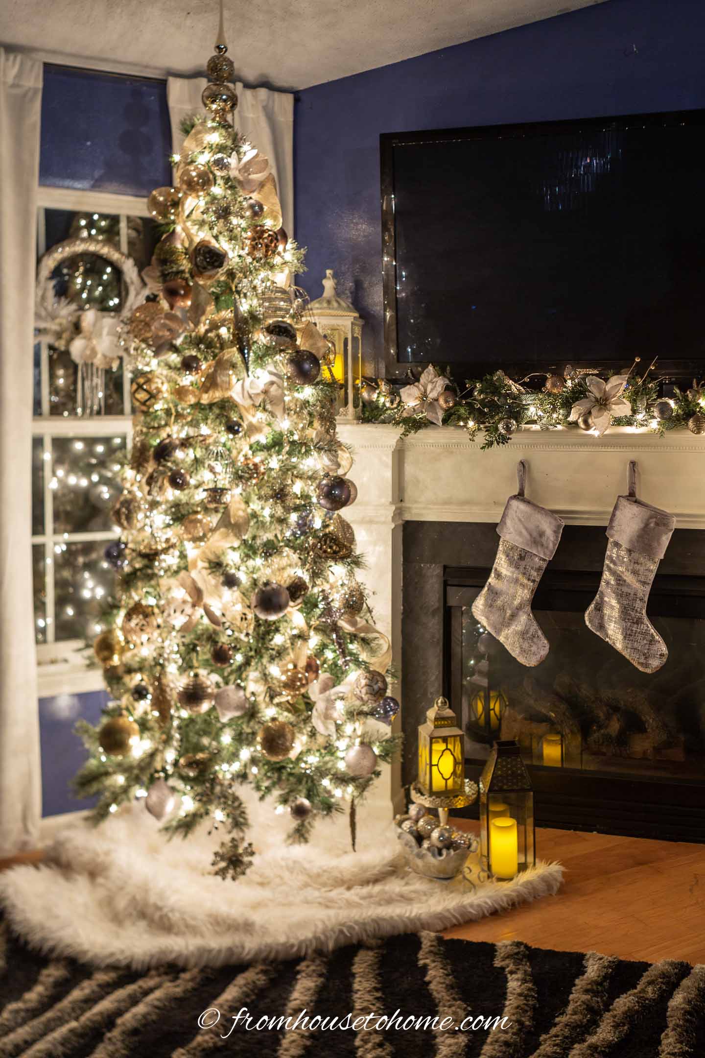 Mixed metals Christmas tree lit up at night beside a fireplace mantel